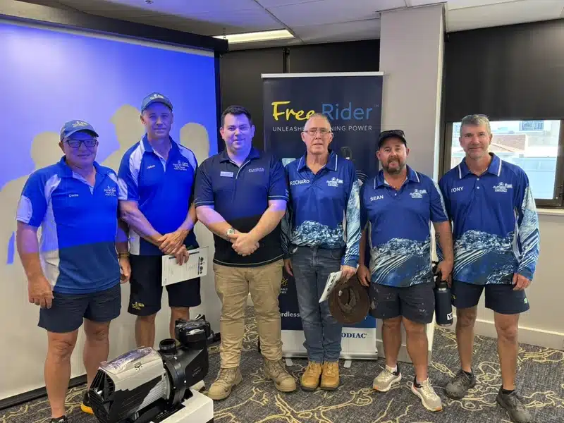 Jim’s Pool Care technicians in branded uniforms at a pool equipment training session with a display pool pump