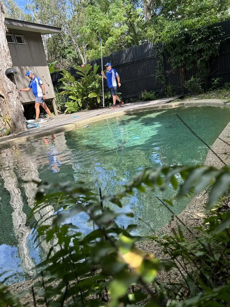 Two Jim’s Pool Care technicians cleaning a natural rock swimming pool surrounded by tropical planting in Townsville