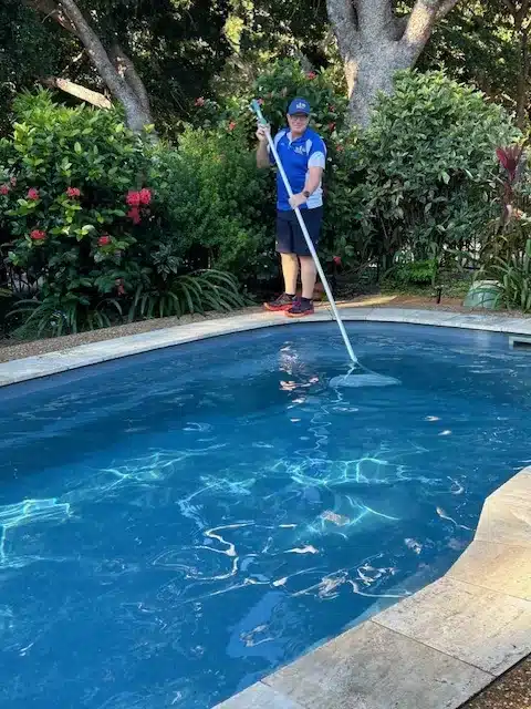 Jim’s Pool Care technician skimming leaves from the surface of a Townsville swimming pool with a leaf rake