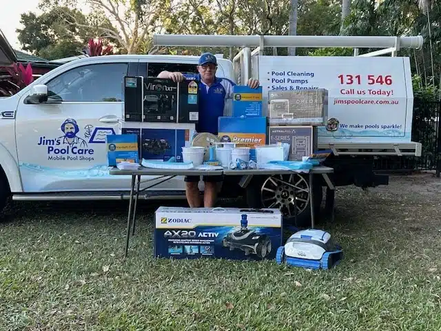 Jim’s Pool Care Townsville technician beside a Mobile Pool Shop van with pool pumps, chlorinators, robotic cleaners and chemicals displayed on a table