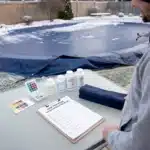 Pool owner with a winter pool maintenance checklist, test kit and chemicals beside a covered pool